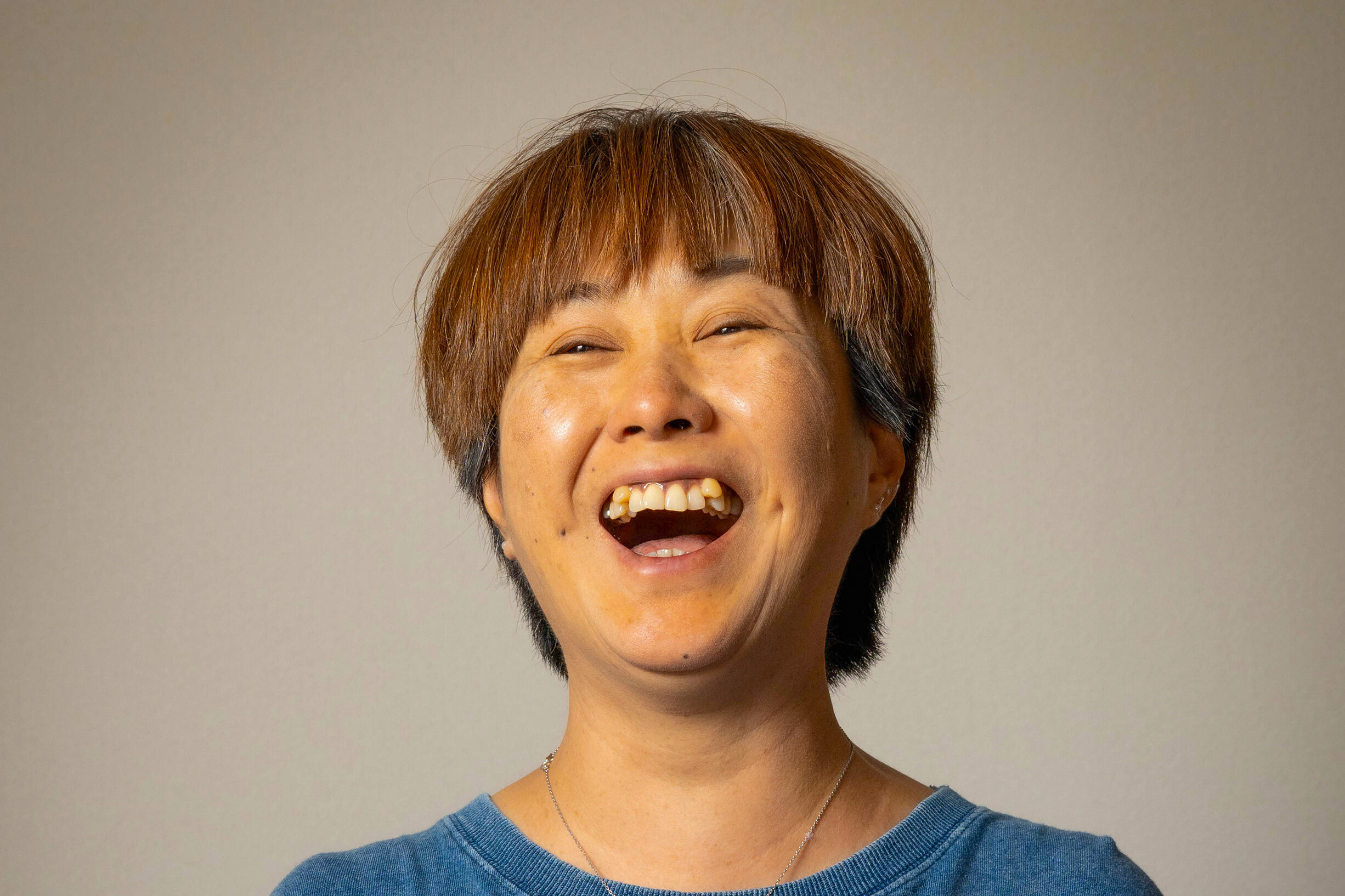 「DESIGN STUDIO FUUが格上のクオリティで捉えた、グレー背景の前で心から楽しそうに大笑いする女性のプロフィール写真」